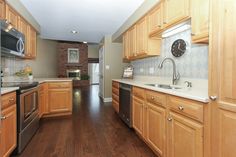 an empty kitchen with wooden cabinets and stainless steel appliances, along with a clock on the wall