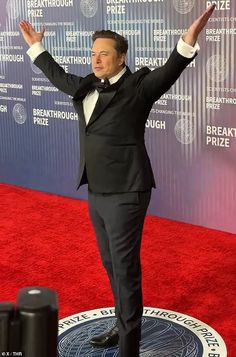 a man in a tuxedo standing on a red carpet with his hands up