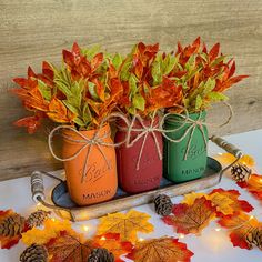 three mason jars with autumn leaves and pine cones in them are sitting on a tray