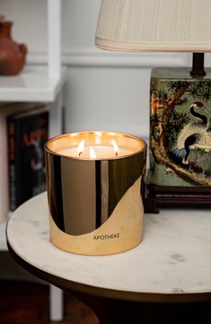 a lit candle sitting on top of a table next to a painting and lamp shade