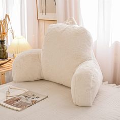 a large white pillow sitting on top of a bed next to a book and lamp