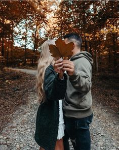 a man and woman holding up a leaf in the middle of a dirt road surrounded by trees