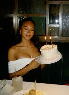 a woman holding a cake with candles on it in front of a plate full of fruit