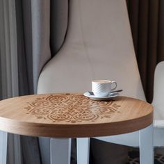 a coffee cup sitting on top of a wooden table next to a white leather chair