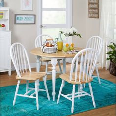 three white chairs around a round table in a room with blue rugs and pictures on the wall