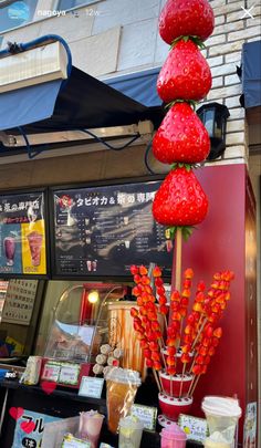 there are many strawberries on display in the store front window and behind it is a vase with red flowers