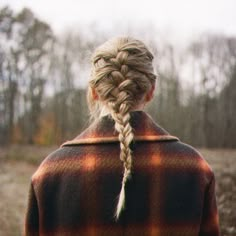 a woman standing in the middle of a field with her hair in a fishtail braid