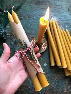 a person holding a lit candle next to some candles and pine cones on a table