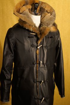 Every coat we make is totally custom. We love to work with deerskin. It has a wonderful buttery texture, a gorgeous and complicated grain, and is durable and stretchy. The coat pictured is sewn from black deerskin for a rustic and rugged look with antler toggles and white top-stitching. The fur on this piece is sheared New Zealand possum (which is not something that we can normally get!) that the client had had tanned and sent to us. The style also features a detachable fur lined hood. The price Fall Leather Hunting Outerwear, Leather Hunting Outerwear For Fall, Fitted Sheepskin Long Coat, Fitted Long Sheepskin Coat, Leather Outerwear For Hunting In Fall, Black Hunting Outerwear For Fall, Black Outerwear For Hunting In Fall, Black Outerwear For Fall Hunting, Winter Hunting Black Outerwear