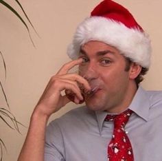 a man wearing a santa hat talking on a cell phone while wearing a red tie