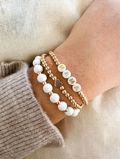 Our new mama bracelets make a great gift to celebrate mom. Gift this to mom to celebrate a new baby, her birthday, or mother's day! Each bracelet set comes with 3 stacked bracelets.  Stack of 3 Beaded Bracelets: ♥ MAMA bracelet with gold beads ♥ Gold Heart shape with gold beads ♥ White wood beads and gold beads   Bracelet is adult Size, one size fits *most* Diameter(Unstretched): 2.5" Add-on to our Mom care Package or our New Parent Gift Box! ------------------------------------------------------------------------------------------------ Care Instructions  Mug: Gentle handwash only. Do not scrub on lettering. Not microwave or dishwasher safe.  Processing Time: Products are made to order after you purchase. Each order takes 1-4 business days to make and ship out. We will start your order af Mom And Me Bracelets, Mama And Me Bracelets, White And Gold Clay Bead Bracelet, Gold Bead Bracelet Stack, Stack Bracelets Beaded, Diy Clay Bead Bracelet, Stretch Beaded Bracelets Diy, Bracelets Stack, Stacked Beaded Bracelets