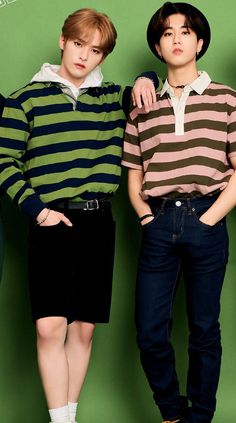 two young men standing next to each other in front of a green wall wearing striped sweaters