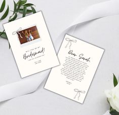 two wedding cards on top of a table next to white flowers and ribbon tied around them