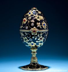 an ornately decorated egg sitting on top of a metal stand in front of a blue background