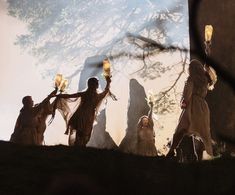 people dressed in medieval costumes holding torches and standing on a hill with trees behind them