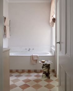 a bath tub sitting next to a window in a white room with checkered flooring