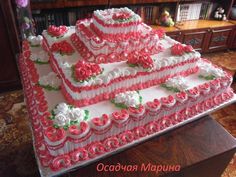 a large cake with pink and white frosting roses on the top is sitting on a table in front of a bookshelf