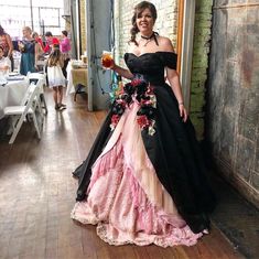 a woman in a black and pink dress standing next to a brick wall holding a drink