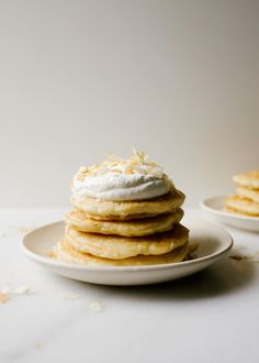 a stack of pancakes with whipped cream on top sitting on a white plate next to each other