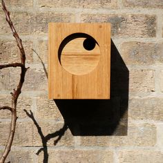 a wooden clock mounted to the side of a brick wall next to a tree branch