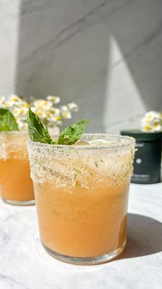 two glasses filled with drinks sitting on top of a white table next to each other