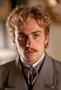 a man with curly hair wearing a gray suit and bow tie looking at the camera