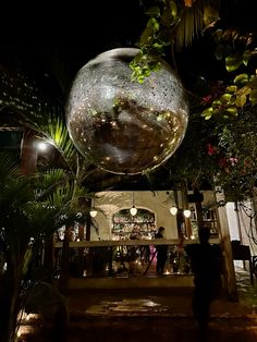 a large disco ball hanging from the ceiling in front of a bar with plants and lights