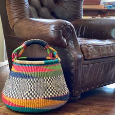 a colorful basket sitting on the floor next to a leather chair in a living room