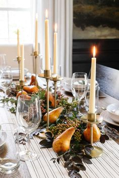 a dining room table set with candles, fruit and greenery on the centerpiece