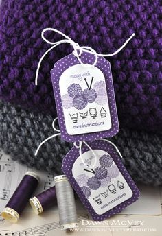 two tags are attached to the back of a purple knitted beanie and some thread