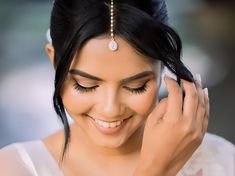 a woman smiles as she holds her hair in one hand and wears a pearl headpiece on the other