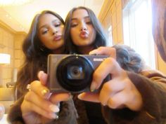 two women taking a selfie in front of a mirror with one holding a camera