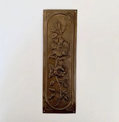 a metal plaque with flowers and leaves on it's side hanging from the wall