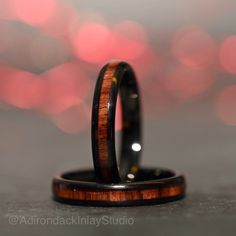 two wedding rings with wood inlays on top of each other, against a blurred background