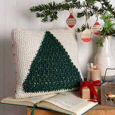 a crocheted christmas tree pillow sitting on top of a table next to an open book