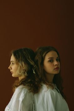 two young women standing next to each other in front of a red wall and one is looking off into the distance