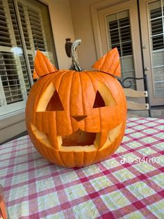 a pumpkin carved to look like a cat sitting on top of a checkered table cloth