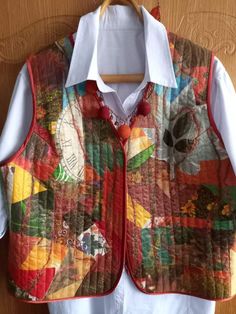 an old quilted vest hanging on a wooden hanger with a white shirt underneath it