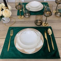 a place setting with white plates and silverware on a green place mat next to gold - plated utensils