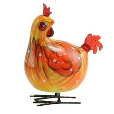 an orange and white glass rooster figurine sitting on top of some black sticks