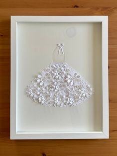 a white dress made out of buttons in a shadow box on a wooden table top