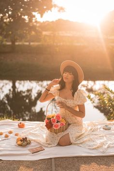 a woman in a hat sitting on a blanket holding a basket with food and drinks