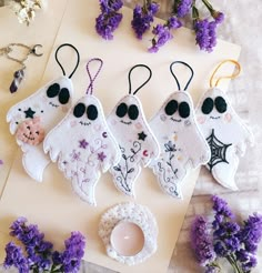 three embroidered ghost ornaments sitting on top of a table next to purple flowers and an egg