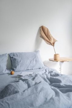 an unmade bed with blue sheets and a wooden lamp on the wall behind it