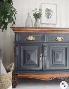 an old dresser is painted gray with gold handles and pulls on the doors, in front of a potted plant