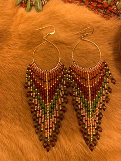 18k dipped gold hoop earrings with earth tone colored beaded fringe hanging from them. At the end of each fringe is a faceted peridot and a red Picasso fire polished crystal. The hoops are attached to gold filled French hooks Bohemian Teardrop Jewelry With Dangling Beads, Festival Dangle Jewelry With Gold Beads, Bohemian 14k Gold-filled Jewelry With Colorful Beads, Beaded Dangle Earrings In Brass, Gold Jewelry With Beaded Fringe For Festival, Elegant Beaded Fringe Jewelry For Festivals, Beaded Brass Dangle Earrings, Brass Beaded Dangle Hoop Earrings, Dangling Bead Tassel Earrings For Festivals