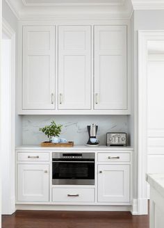 a kitchen with white cupboards and an oven in the center is seen from across the room