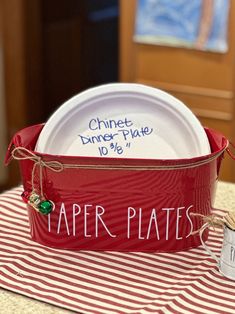 a red bucket with paper plates in it sitting on a table next to a white plate