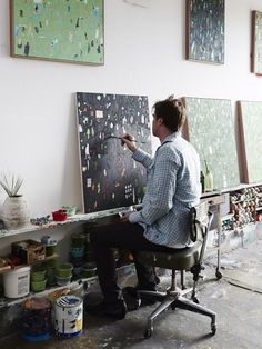 a man sitting at a desk painting on canvases