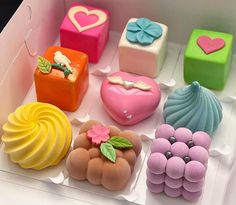 there are many different types of cakes in the display box, each decorated with flowers and hearts